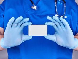 Der männliche Arzt mit blauen Latexhandschuhen hält eine leere Visitenkarte aus weißem Papier foto