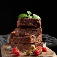 Stapel gebackener quadratischer Stücke Schokoladenkuchen auf braunem Holzschneidebrett foto