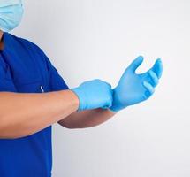 männlicher arzt in blauer uniform zieht sich vor der operation weiße sterile latexhandschuhe an foto