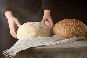 zwei weibliche hände lagen auf einem tisch gebackenes weißes rundes brot aus weißem weizenmehl foto