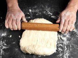 Koch in einer schwarzen Tunika rollt einen Teig für eine runde Pizza foto