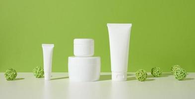Glas, leere weiße Plastikrohre für Kosmetika auf einem weißen Tisch, grüner Hintergrund. Verpackungen für Creme, Gel, Serum, Werbung und Verkaufsförderung foto