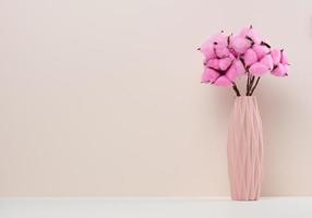 rosa keramikvase mit rosenbaumwollblumenstrauß auf weißem tisch foto