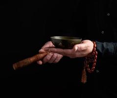 Mann in einem schwarzen Hemd dreht einen Holzstab um eine tibetische Kupferschüssel. Ritual der Meditation foto