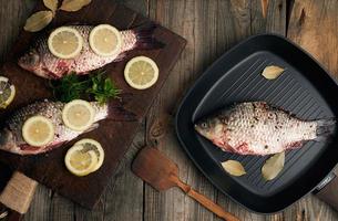 Frischer Fisch in Karauscheschuppen auf einem braunen alten Holzschneidebrett, mit Gewürzen gewürzte Speisen foto