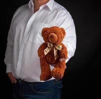erwachsener mann in einem weißen hemd hält einen braunen teddybären foto