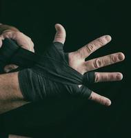Der Mann wickelt seine Hände in einen schwarzen Textilverband für den Sport foto