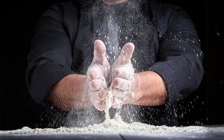 Koch in schwarzer Uniform gießt weißes Weizenmehl aus seinen Händen foto