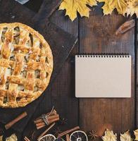 Gebackener Apfelkuchen auf einem Brett und ein Notizbuch mit einer leeren Seite zum Schreiben eines Rezepts foto