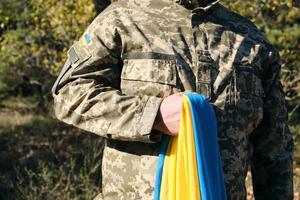 Der ukrainische Soldat hält die gelb-blaue Flagge des Staates in der Hand, er drückte seine Hand auf seine Brust foto