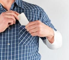 Mann in einem blauen Hemd steckt eine leere Visitenkarte aus weißem Papier in die Tasche foto