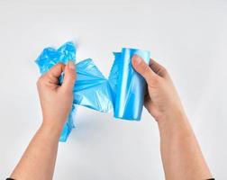 Frauenhände reißen eine transparente blaue Tasche für einen Mülleimer von einer Rolle ab foto