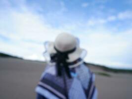 unscharfes Foto einer Frau mit Hut am tropischen Strand, die zum Himmel und zum Meer blickt