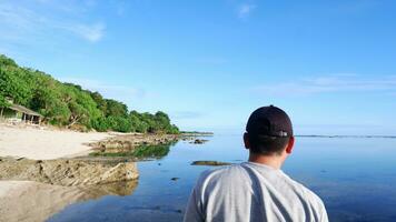 Rückseite eines Mannes mit Hut, der auf die blauen Strände, Inseln und den wunderschönen blauen Himmel blickt foto