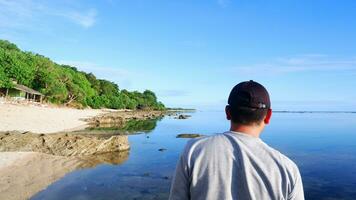 Rückseite eines Mannes mit Hut, der auf die blauen Strände, Inseln und den wunderschönen blauen Himmel blickt foto