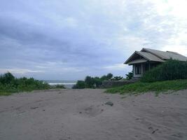 Blick auf das Haus in den Dünen von weißem Strand, grünes Gras und strahlend blauer Himmel am tropischen Strand von Indonesien, Panoramablick foto