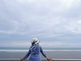 Rücken der Frau mit Hut am tropischen Strand, die von der Brücke aus auf den Himmel und das Meer blickte. Seeblick foto