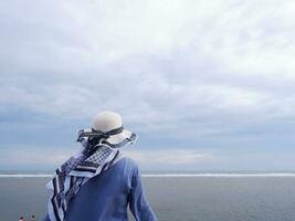 Rückseite der Frau mit Hut am tropischen Strand, die zum Himmel und zum Meer blickt foto