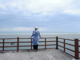 Rücken der Frau mit Hut am tropischen Strand, die von der Brücke aus auf den Himmel und das Meer blickte. Seeblick foto