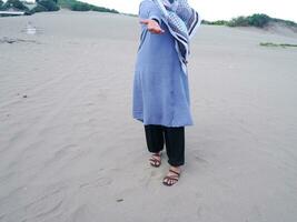 Der halbe Körper der Frau in Blau stand auf dem Strandsand und ihre Hände waren nach vorne offen erhoben foto