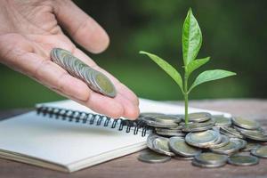 hand, die einem baum, der aus einem stapel von münzen wächst, eine münze gibt. finanzbuchhaltung, anlagekonzept. foto