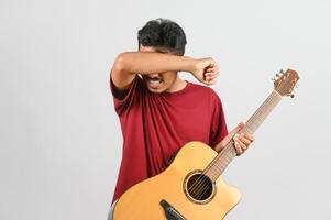 Porträt des jungen asiatischen Mannes im roten T-Shirt mit einer akustischen Gitarre, die auf weißem Hintergrund isoliert ist foto