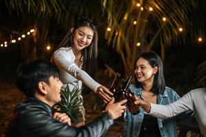 porträt glücklicher asiatischer freunde, die zusammen eine dinnerparty haben - junge leute sitzen am bartisch und toasten biergläser abendessen im freien - leute, essen, trinken lebensstil, neujahrsfeierkonzept. foto