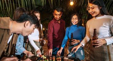 glückliche asiatische freunde, die mit grillabendessen im freien jubeln - gruppe von leuten, die spaß auf der neujahrsparty haben. menschen, essen und trinken lifestyle-konzept nachtparty, menschen und feierkonzept. foto