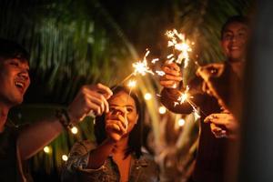 porträt einer glücklichen asiatischen gruppe von freunden, die spaß mit wunderkerzen im freien haben - junge leute, die sich nachts mit feuerwerk amüsieren - menschen, essen, trinken, lebensstil, neujahrsfeierkonzept. foto