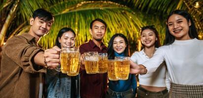 porträt glücklicher asiatischer freunde, die zusammen eine dinnerparty haben - junge leute, die biergläser abendessen im freien anstoßen - menschen, essen, trinken lebensstil, neujahrsfeierkonzept. foto