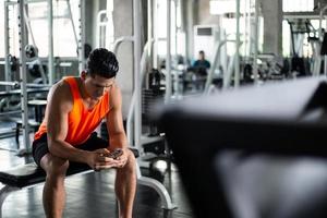 athletischer mann entspannt sitzen und sms-nachricht auf dem smartphone bei fitness foto