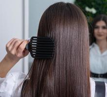 junge frau, die ihr langes dunkles haar mit einem kamm in einem schönheitssalon kämmt. ein glattes, gesundes, brünettes Haar, das der Haarglättung unterzogen wurde. foto