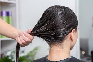 Friseur wendet eine Haarmaske auf glattes schwarzes Haar an. Haarpflege im Schönheitssalon. foto