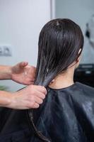 Friseur wendet eine Haarmaske auf glattes schwarzes Haar an. Haarpflege im Schönheitssalon. foto