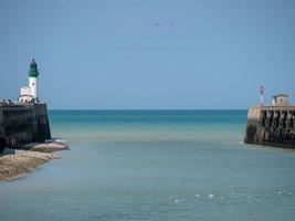 Menschen am Pier neben Leuchtturm und Gewässer unter klarem blauem Himmel in Frankreich foto