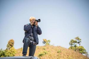 junger Fotograf, der auf seinem Kleintransporter sitzt, der einen Berg fotografiert foto