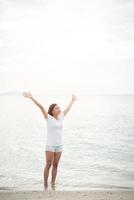 junge schöne Frau streckt ihre Arme in der Luft am Strand mit bloßen Füßen foto