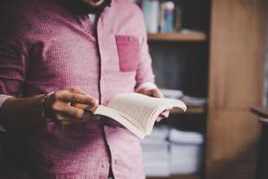 junger Hipster-Mann, der Buch in einer Bibliothek liest foto