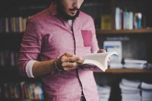 junger Hipster-Mann, der Buch in einer Bibliothek liest foto