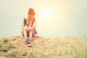 junge Hipsterfrau, die auf dem Sand sitzt und Rucksack trägt, der so traurig fühlt foto