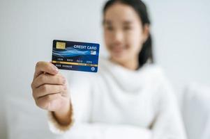 junge Frau mit einer Kreditkarte, die auf Bett lächelt foto