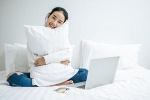 junge Frau sitzt auf ihrem Bett und umarmt Kissen