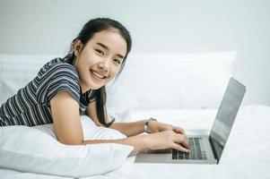 eine Frau in einem gestreiften Hemd spielt auf ihrem Laptop auf ihrem Bett
