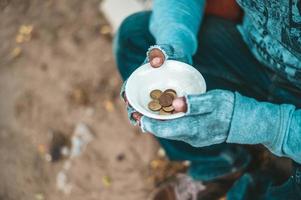 Obdachloser sitzt mit einer Tasse Geld foto