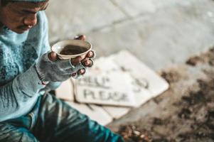 Bettler sitzt unter einer Brücke mit Tasse für Geld foto