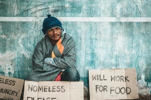 Mann sitzt neben der Straße mit einer obdachlosen Nachricht foto