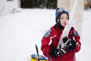 Junge leckt im Winter einen Eiszapfen mit der Zunge. foto