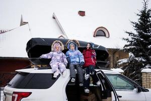 Drei Kinder sitzen im Winter auf einer Autodachbox gegen Haus. foto