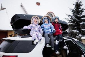 Drei Kinder sitzen im Winter auf einer Autodachbox gegen Haus. foto