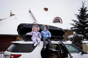 Zwei Schwestern sitzen im Winter auf einer Autodachbox gegen Haus. foto